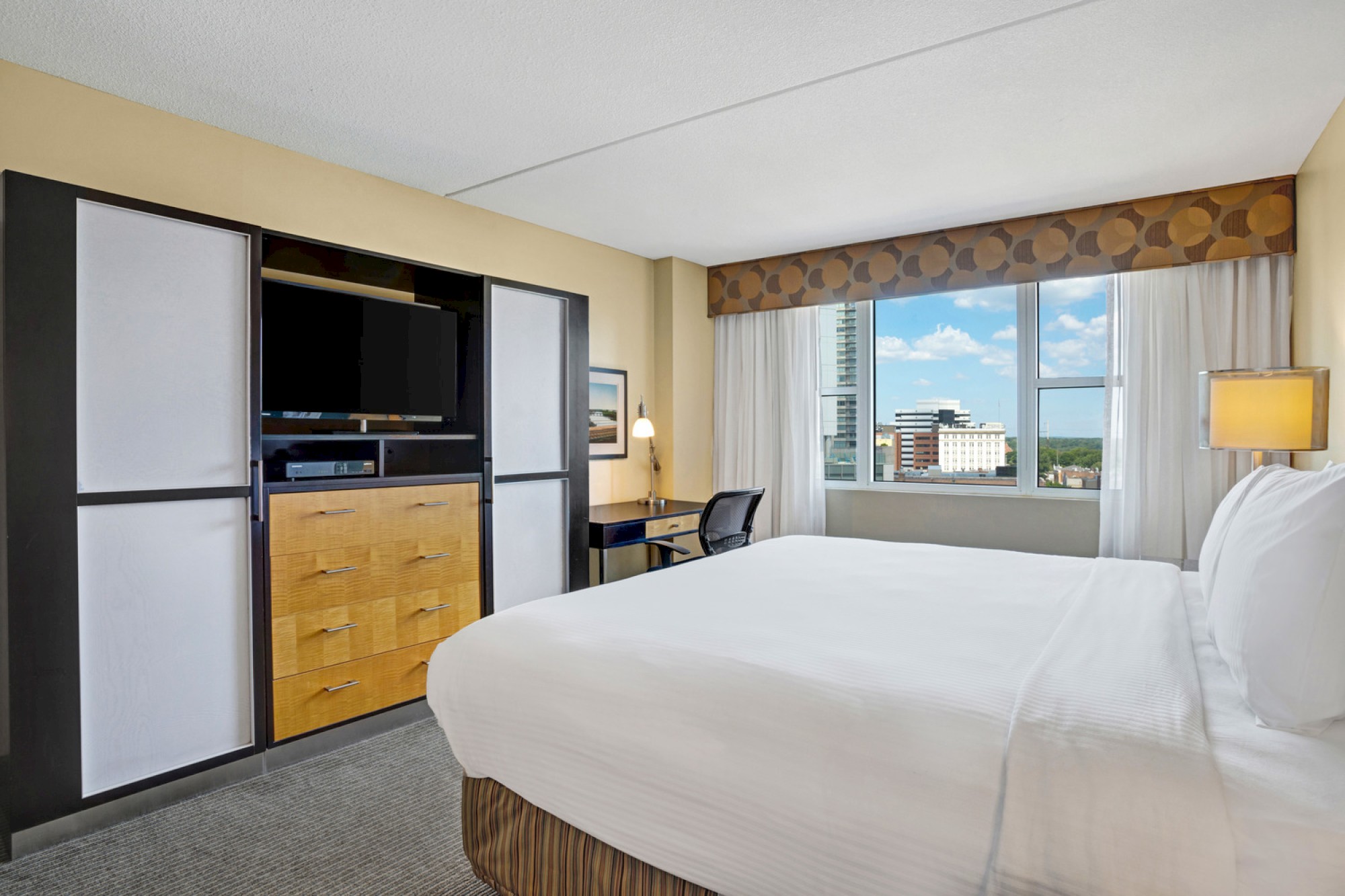 Photo of luxury modern hotel room with king size bed, tv in front of it and big window with curtains