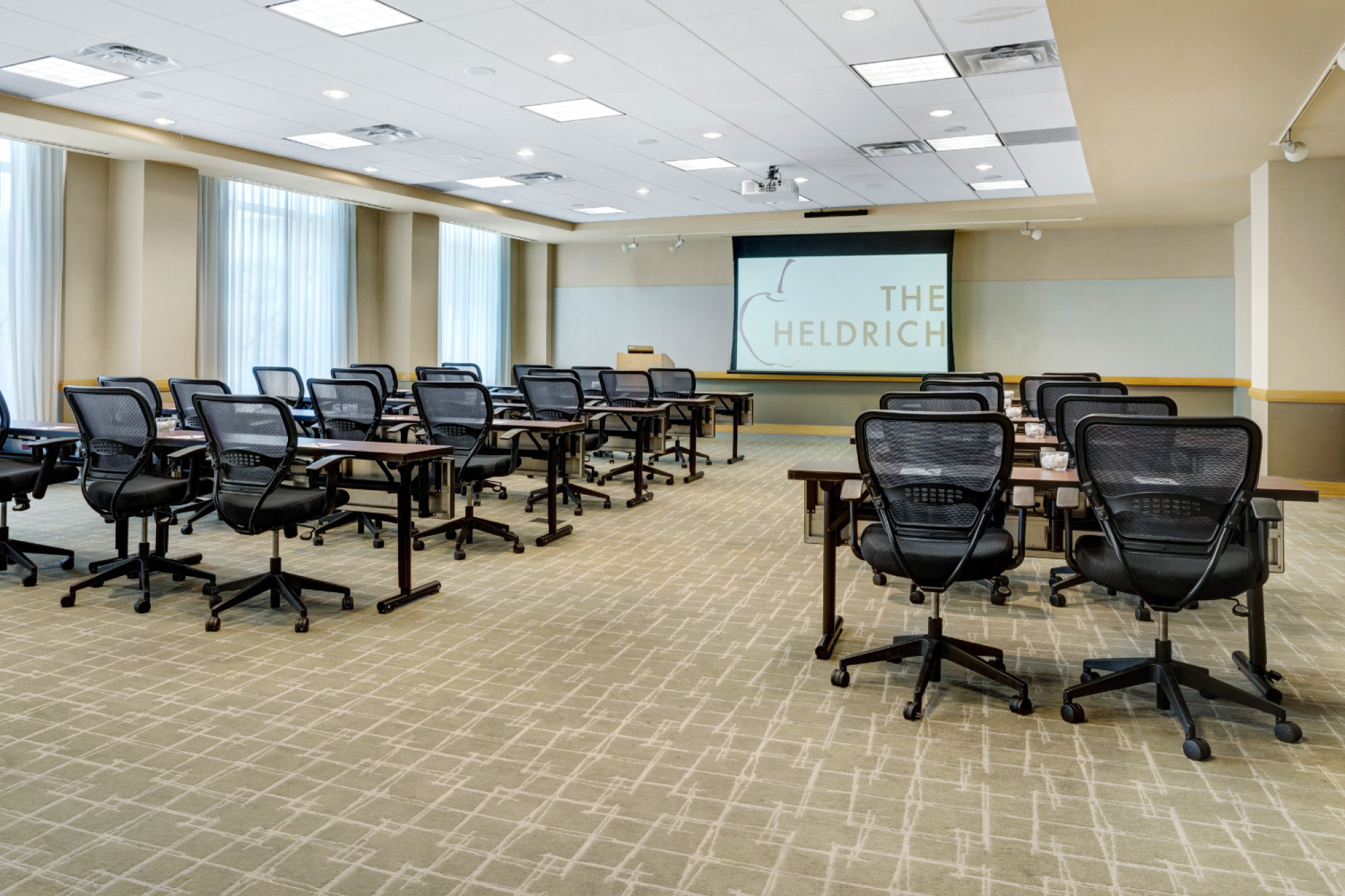 Photo of meeting room in school set up with black wheeled chairs, multiple windows and a white screen to project in the back of the meeting room