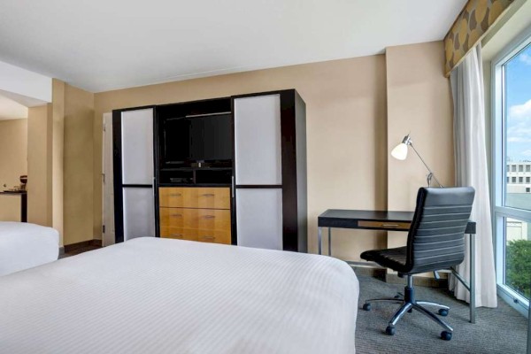 Photo of luxury modern hotel room with double beds, tv in front of it and big window with curtain and desk set up in front of it