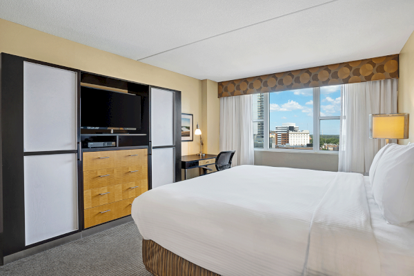 Photo of luxury modern hotel room with king size bed, tv in front of it and big window with curtains