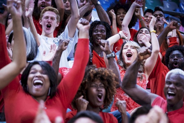 Photo of multiple people cheering a team all dress in red clothing and raising their hands with a happy expresion