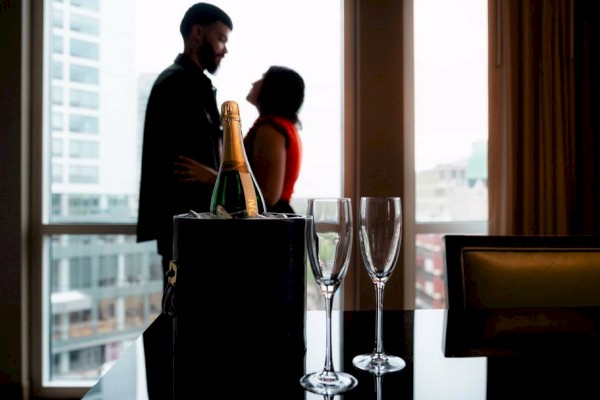 Photo of a couple in the back or a room in front of the window, with glasses of champage and champage on the table