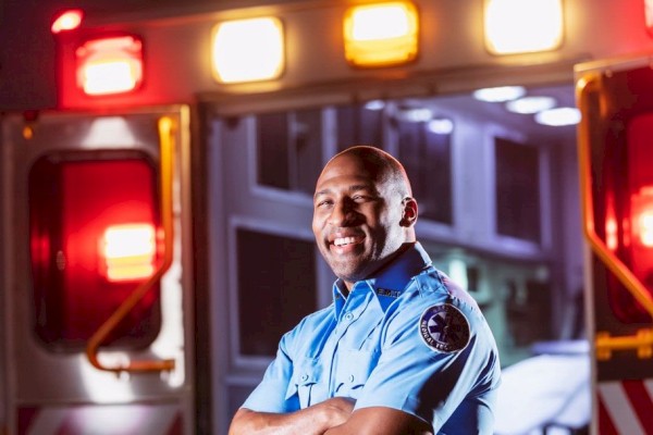 Photo of first responder person with his arms cross smiling and posing in front of an ambulance