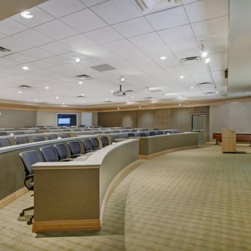 Photo of meeting room in auditorium set up with black wheeled chairs and a white screen to project in the right