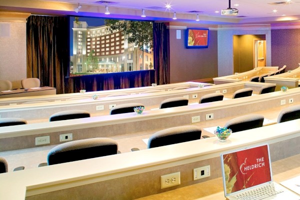 Photo of meeting room in auditorium set up with black wheeled chairs and a white screen to project in the back of the room