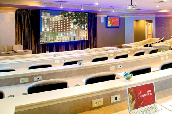 Photo of meeting room in auditorium set up with black wheeled chairs, multiple windows and a white screen to project in the back of the meeting room