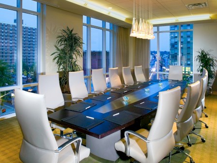 Photo of natural lighted and full windows around boardroom set up with multiple white chairs and an elegant black table