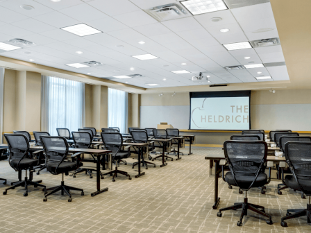 Photo of meeting room in school set up with black wheeled chairs, multiple windows and a white screen to project in the back of the meeting room