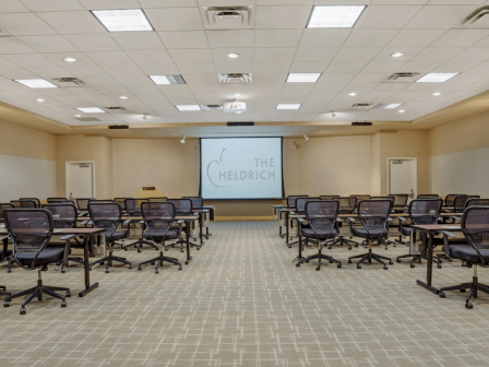 Photo of meeting room in school set up with black wheeled chairs, multiple windows and a white screen to project in the back of the meeting room