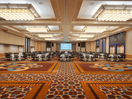 photo of carpeted empty ballroom with multiple ceiling lamps and a few chairs and tables in the back of the room