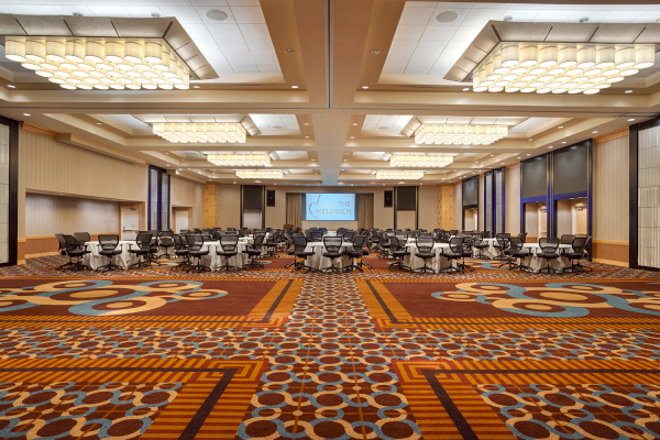 Photo of empty carpeted ballroom with multiple chairs and tables in the back of the meeting room