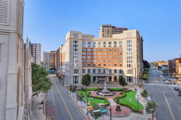 Photo of The Heldrich façade with green grass and statue plaza in front of it and incoming traffic on both sides