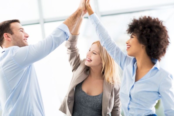 three people raising their hands doing a high five in business attire in a lighted room