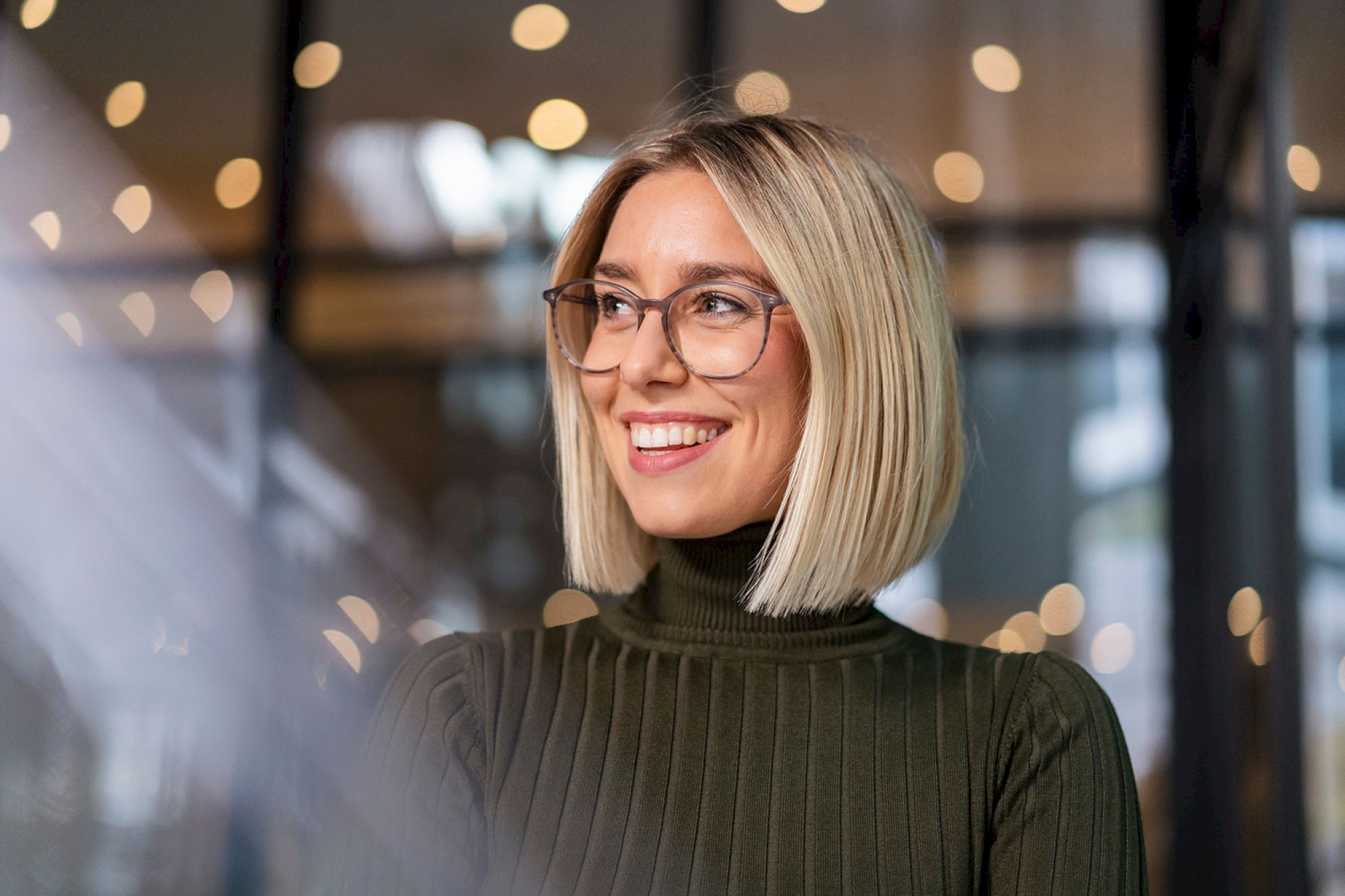 close portrait of business blonde woman wearing glasses in a black turtle neck inside building