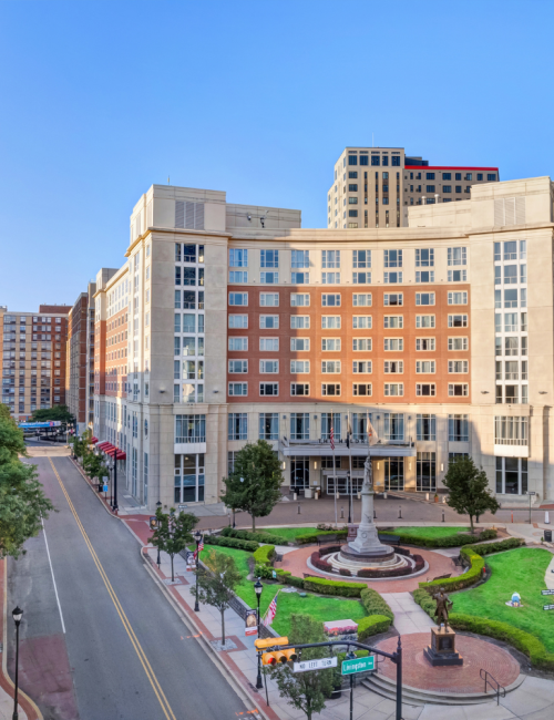 photo of The Heldrich hotel façade with green grass area and statue plaza in front of it with traffic in comming from both sides