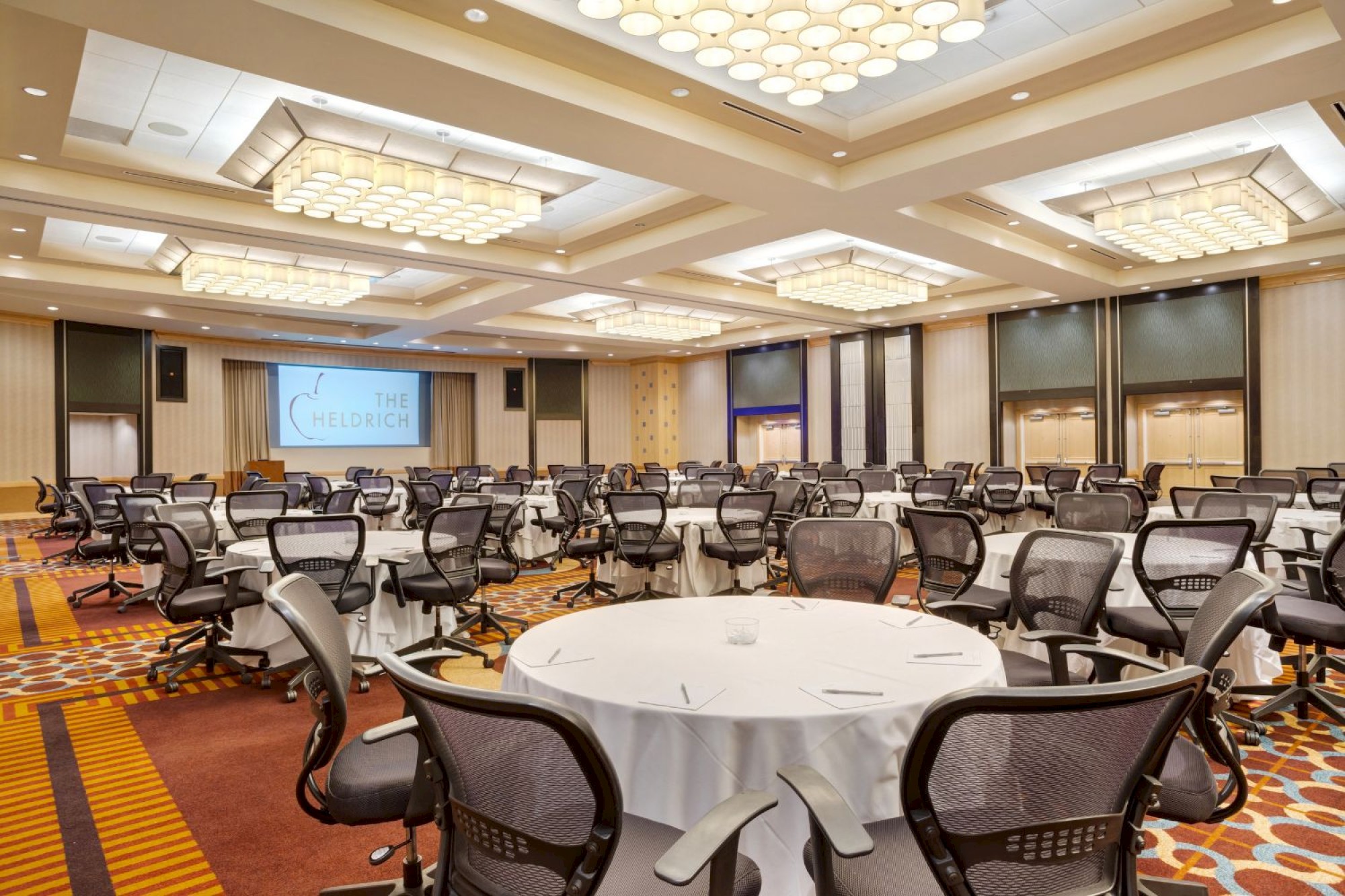 Photo of meeting room in cabaret or round set up with black wheeled chairs, multiple windows and a white screen to project in the back of the meeting room