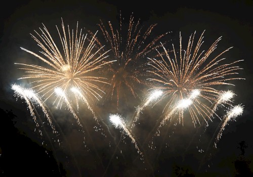 The image shows a vibrant fireworks display against a dark sky, featuring golden bursts and bright white trails creating a celebratory scene.