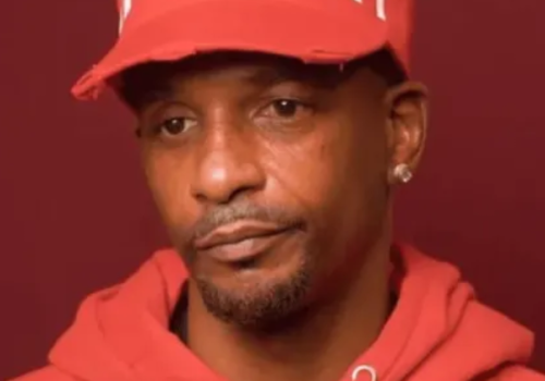 A person wearing a red hoodie and cap, with a neutral expression, against a dark red background.