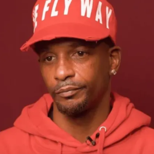 A person wearing a red hoodie and cap, with a neutral expression, against a dark red background.