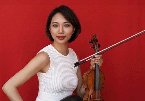 A person in a white dress holding a violin against a bright red background.