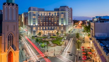 Night Photo of The Heldrich hotel Façade with green grass and statue plaza in front of it, and incoming traffic from both sides