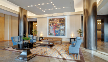 Photo of luxury modern hotel lobby with lounge chairs and a table in a marble-ish floor with modern ceiling lights and metallic collumns