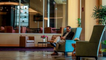 Photo of luxury modern hotel lobby with main sitting in lounge chairs and a table in a marble-ish floor