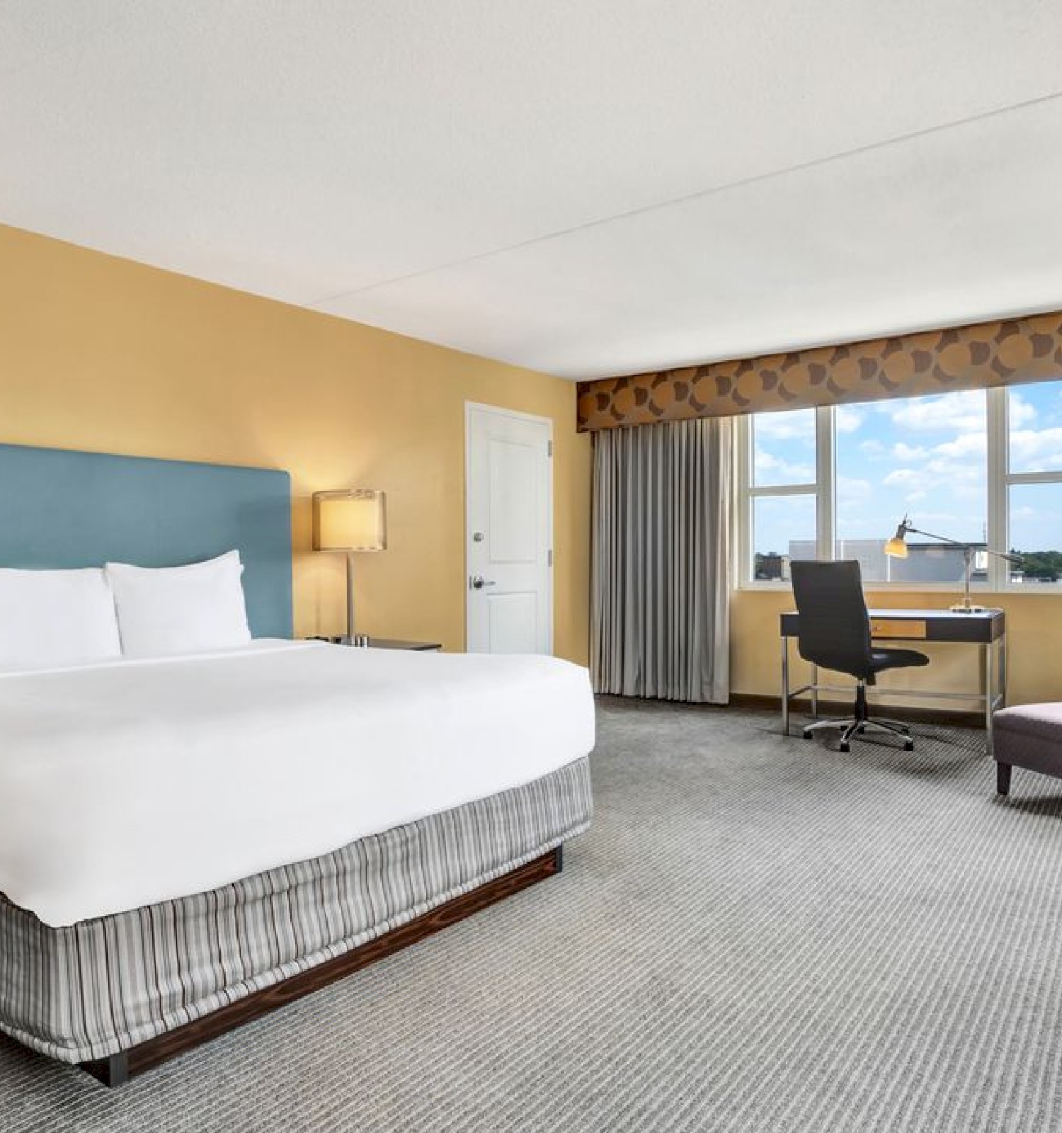 Photo of luxury modern hotel room with king size bed and big window with curtains and desk set up in front of it