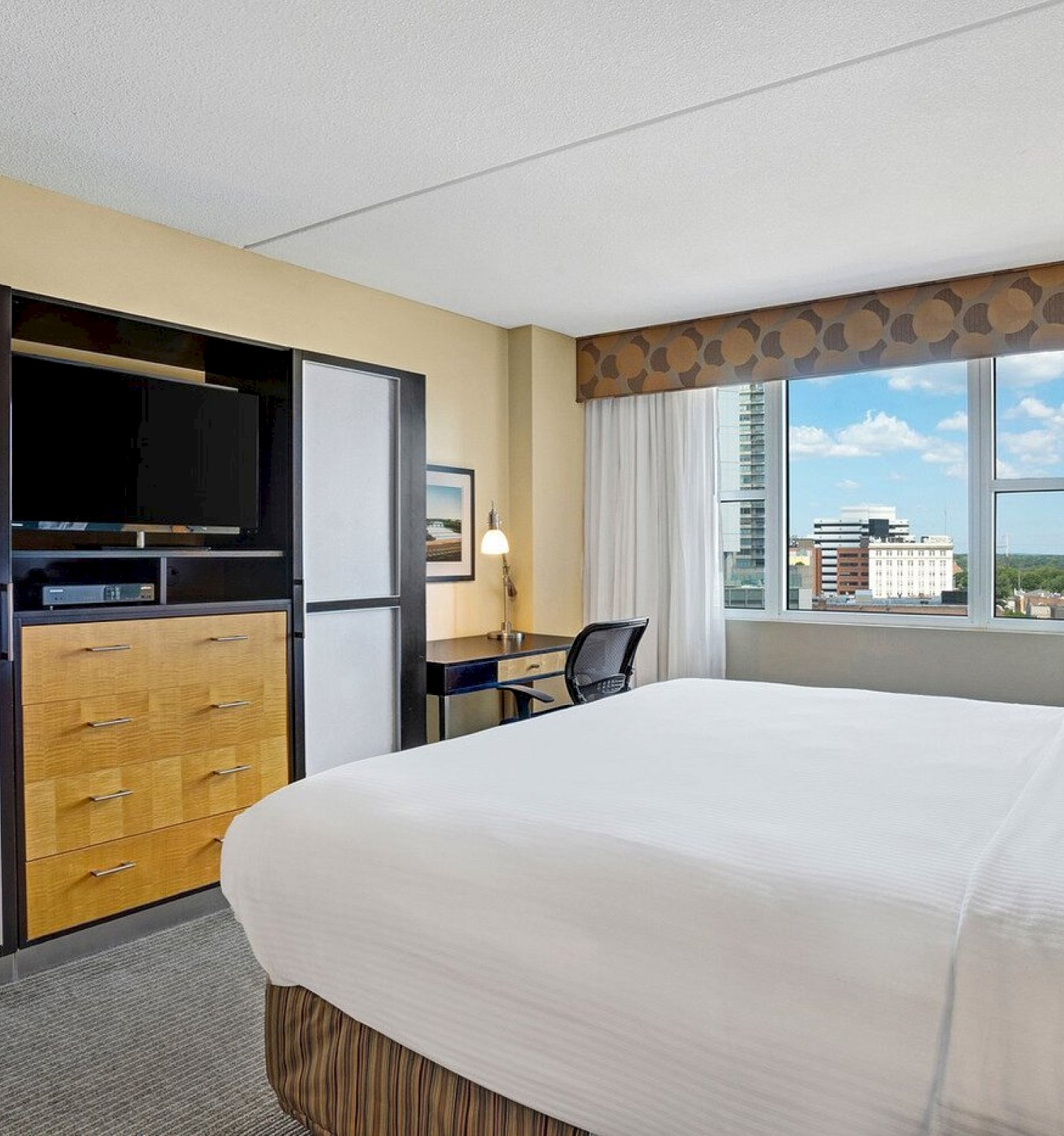 Photo of luxury modern hotel room with king size bed, tv in front of it and big window with curtains