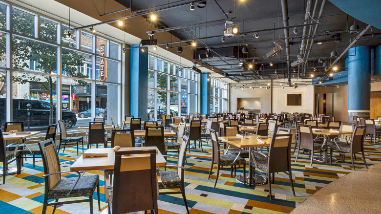 Photo of restaurant with multiple windows, chairs and tables in a colorful floor