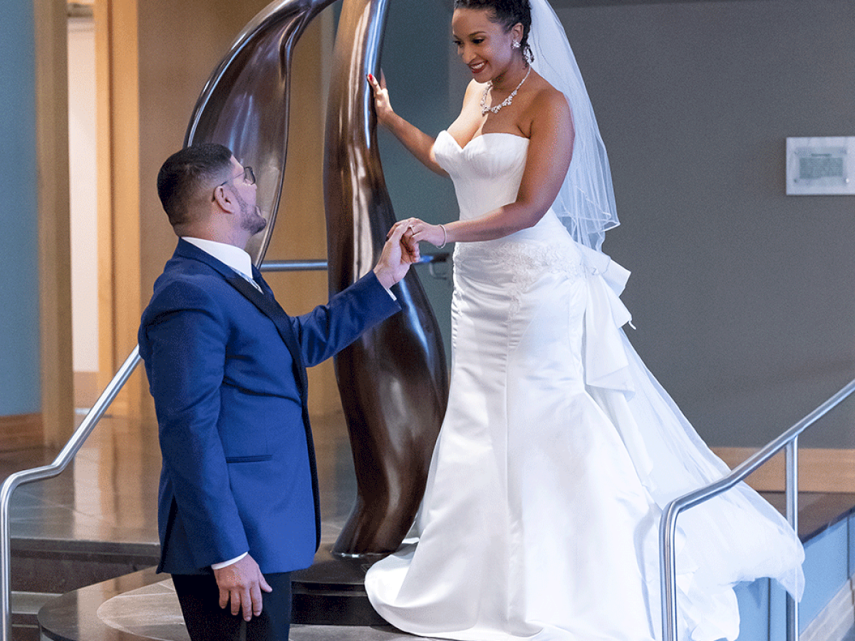 Photo of a bride on top of an sculpture giving the hand to the groom while they look at each other