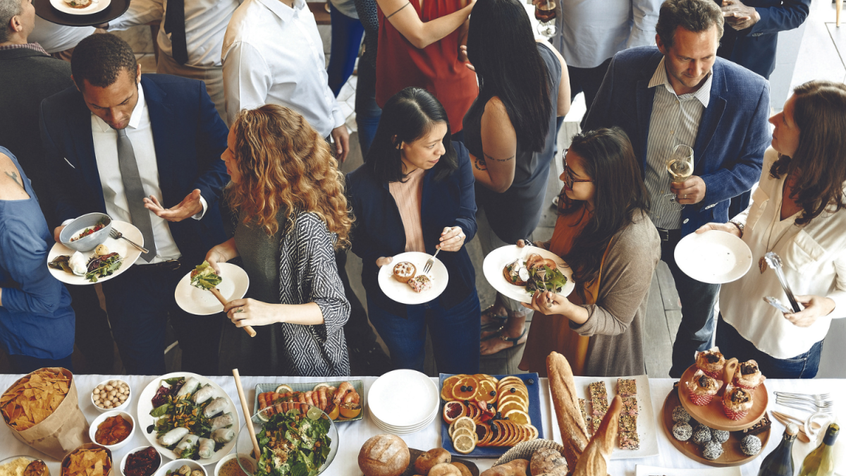 Photo of meeting food event with multiple people chatting dressed in business casual with a buffet table set up