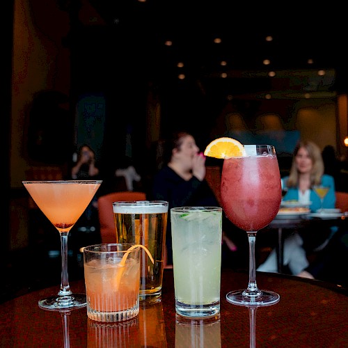 Four drinks on a table in a dimly lit lounge, with people chatting in the background.