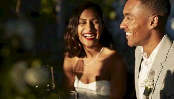 A happy couple, dressed elegantly, smiling and enjoying a moment together outdoors.